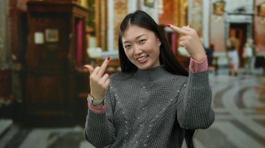 Kadın, kilise ortamında neşeli bir ifadeyle kapalı mekanda jest yapıyor, geleneksel mimariyi çağdaş modayla harmanlıyor, kültürel birlikteliği ve kişisel ifadeyi ön plana çıkarıyor..