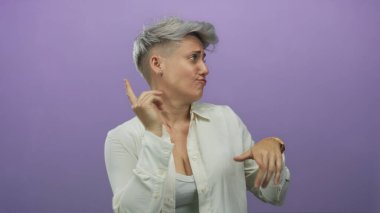 Parmakla işaret eden, gülümseyen yüzlü ahşap saat takan ve mor stüdyoda kendini ifade eden elleri olan bir kadın..