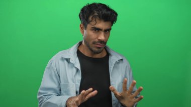 Genç İspanyol adam, yeşil stüdyoda avuçlarıyla ve çatık kaşlarıyla duraksamayı başarıyor..