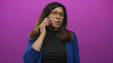 Mavi ceketli İspanyol kadın, stüdyoda akıllı telefonu kulağına tutarken yan profili öne eğiyor..