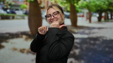 Güneşli bir günde, gülümseyen ve işaret eden bir kadın gözlük ve siyah bir ceket takıyor..