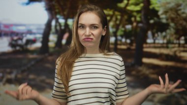 Çizgili gömlekli kadın, parlak güneş ışığı altında meşe ağaçlarının yanındaki yeşil parkta el ve kırışıklıklar silkeliyor..