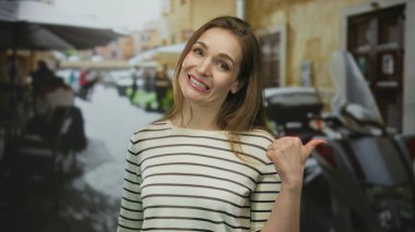 Beyaz kadın gündüz vakti kalabalık şehir caddesinde gülümseyip başparmağıyla işaret ediyor..