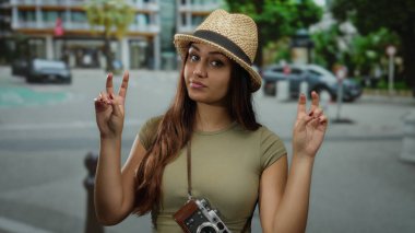 Hasır şapkalı kadın iki eliyle şehir sokağında barış işareti yapıyor. Kameralar sallanıyor, gençlik ruhu sergiliyor..