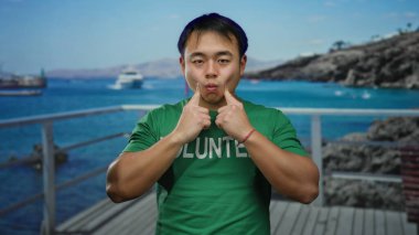 Yeşil tişörtlü bir adam deniz kenarındaki sahil yolunda resimli bir şekilde poz veriyor..