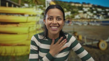 Deniz kıyısında gülümseyen genç İspanyol kadın. Sarı kanoları ve güneşli bir gökyüzünün altında canlı bir açık hava manzarası var.