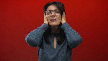 Kırmızı stüdyoda kulaklarını kapatırken, kederli bir ifadeyle yüzünü buruşturan orta yaşlı İspanyol kadın;.