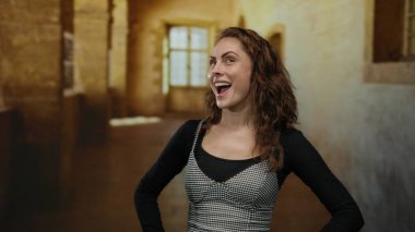 Yaşlı bir üniversite koridorunda gülümseyen genç bir kadın. Büyük pencerelerden içeri güneş ışığı giriyor. Sıcak ve sıcak bir atmosfer yaratıyor..