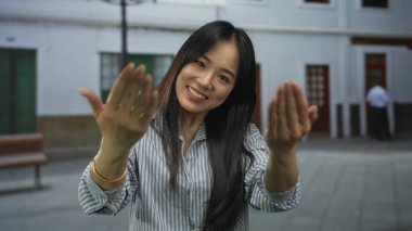 El kol hareketi yapan genç Çinli kadın, sokak ortasında gülümseyerek şehir yaşamının neşeli özünü yakalıyor..