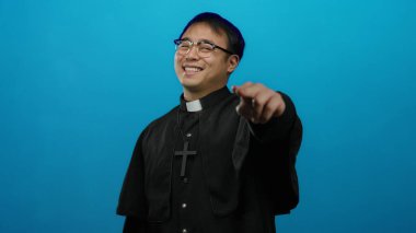 Mavi arka plana poz veren rahip kıyafeti giyen adam güven verici bir dini kavrama işaret ediyor. Jest ve ifade yoluyla güven ve inanca ilham veriyor..