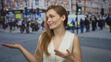 Kadın, diğer eliyle çağrı jesti yaparken el hareketleriyle sokakta açık el kol hareketi yapar; şaşkınlık merak belirsizliği şüphesi.