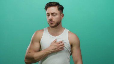 Beyaz kolsuz tişörtlü genç adam, izole edilmiş yeşil arka plan duvarına karşı düşünceli ve düşünceli bir görünüm sergiliyor..