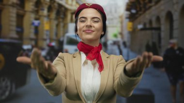 Üniformalı bir kadın, hareketli bir şehir caddesinde gülümseyerek ve jestler yaparak neşeli bir tavır takınıyor, profesyonellik ve samimiyet sergiliyor..