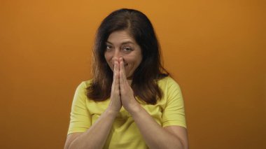 Kadın dua eden eller stüdyoda turuncu bir duvarla, ince bir gülümseme ile sarı bir gömlek giyerek hareket; umut.