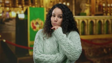 Genç İspanyol bir kadın kilisenin içinde, etrafı kutsal dekorla çevrili, rahat bir süveter giymiş, bir an yansımasını yakalıyor..