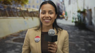 Elinde mikrofon tutan kadın muhabir. Sokak ortamında ABD bayrağı renkleriyle rozet, İspanyol asıllı, gençlerin vatandaşlık sözleşmesini ve açık hava gazeteciliğini gösteren.