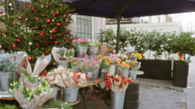 Bulanık Londra sokak sahnesi, kışın çiçeklerle süslenir. Renkli düzenlemeler bir dükkanın dışındaki metal kovalarda sergilenir. Arka planda bokeh etkisi yaratır.