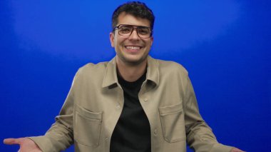 Adam bir stüdyoda omuz silkmek için elini kaldırıyor. İçinde Latin kökenli bir adam resmi var. Düşünme havasında..