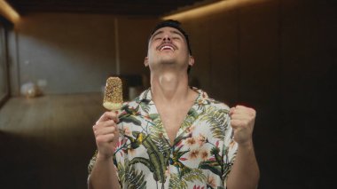 Genç adam tropikal bir tişört giyip otelde dondurma yemekten hoşlanıyor..