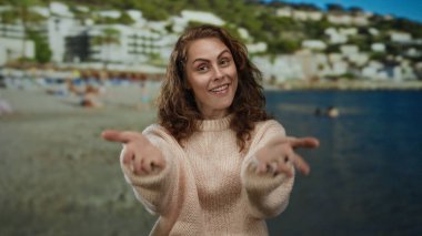 Hareketli bir sahil sahilinde gülümseyen bir kadın açık mavi bir gökyüzünün altında insanlarla dolu rahat bir süveter ve tepeler giyiyor..