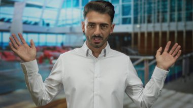 Kıtır beyaz tişörtlü genç İspanyol adam güneş ışığında açık avuçlarıyla iki elini kaldırıyor; belirsizlik..