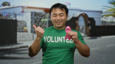 Pembe kurdeleli ve gönüllü tişörtlü genç adam, şehir sokaklarında meme kanseri farkındalığını destekliyor.