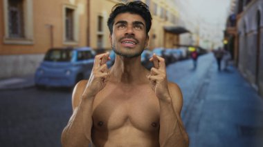 Tişörtsüz genç İspanyol adam umut dolu bir hareketle şehir caddesinde bulanık arabaları ve sıcak güneş ışığında binaları olan umut dolu bir jest yapıyor..