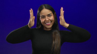 Kadın yüz çerçeveleme arka planda şık, genç Latin Latin kökenli izole edilmiş mavi duvar portresi yaratıyor. Bu portre etkileyici bir sırıtış ve kendine güvenen bakışları vurguluyor..