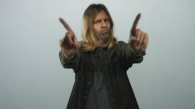 Sarışın, uzun saçlı ve ciddi ifadeli bir adam stüdyoda gri arka planı olan birini işaret ediyor, reddediyor..