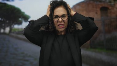 İspanyol kadın, tarihi taş patika ve kırsal mimari arasında stres ifade ederek, eski bir kasaba caddesinde hayal kırıklığına uğramış bir şekilde duruyor..