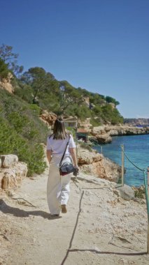 Mallorca 'daki Cala Lombars plajını keşfeden kadın berrak Akdeniz suları ve güneşli bir gökyüzünün altındaki kayalık uçurumlar ile İspanya' da güzel ve huzurlu bir yaz manzarası yaratıyor..