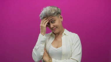 Pembe stüdyoda eli alnında kısa saçlı bir kadın diğer kolunu göğsünde kıvırarak tutuyor..