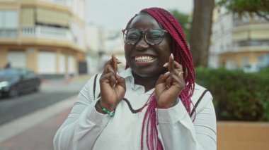 Pembe örgülü bir kadın, şehir sokaklarında neşeyle gülümsüyor, iyimserliğini ve iyimserliğini dile getiriyor..