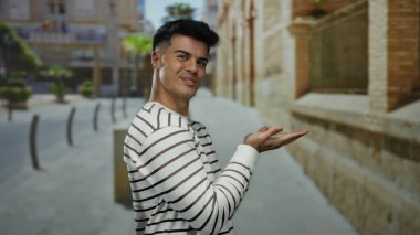 Canlı bir şehir caddesinde uzanmış ellerini uzatarak gülümseyen İspanyol adam, şehir yaşamını ve açık hava cazibesini çekici ve çekici bir şekilde sergiliyor..