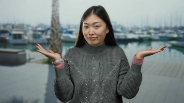 Arka planda tekneleri olan, sakin bir liman manzarasında sakin bir süveter ve izle gülümseyen, sakin bir kadın..