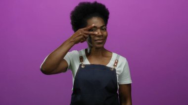 Önlük takan gülümseyen kadın pembe arka planda barış işareti yapıyor, pozitiflik ve stil gösteriyor..