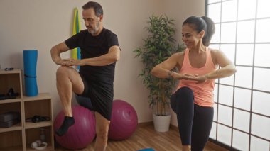 Orta yaşlı İspanyol çift, yoga topları ve bitkilerle birlikte spor salonunda birlikte egzersiz yapıyor. Kapalı alanda, zarif bir şekilde dengede duran bir erkek ve kadınla sevgi ve zindelik sergiliyorlar..