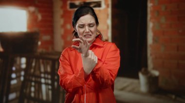 İnşaat alanında turuncu tulumlu bir kadın tamamlanmamış tuğla binada bileğinden rahatsız oluyor..