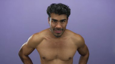 Latin asıllı genç adam mor stüdyoda çıplak göğüs ve ellerle öne eğiliyor; fiziksel rahatsızlık..