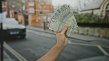 Bir şehir caddesinde Endonezya rupia banknotları tutan bir adam, açık şehir ortamında para gösteriyor..