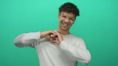 Gözlüklü, beyaz tişörtlü, parmak gösteren ve stüdyoda el kalbi şekli oluşturan bir adam..