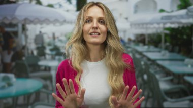 Kadın, genç bir sarışının teras manzarasından hoşlandığı restorandaki servisi durdurmak için ellerini kaldırıyor..