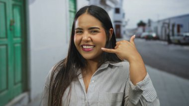 Sokak ortasında genç Latin kökenli Latin havası olan ve şehir zemininde gülümseyen bir kadın el sallıyor..