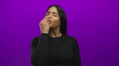 Hisse senedi görüntüsünde, mor arka planda izole edilmiş genç Latin Latin kimliğini vurgulayan, el kaldırılmış şef öpücüğü veren bir kadın yer alıyor..