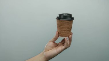 Adamın elinde kahverengi kağıt kahve fincanı beyaz arka planda, çevre dostu tasarım ve minimalist ayarlarda beyaz ten rengini vurguluyor..
