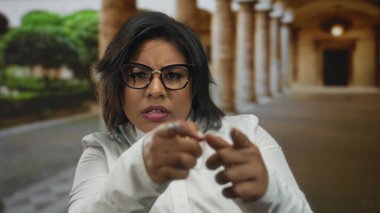 Latin bir kadın üniversitede kuşkuyla işaret ediyor kemer ve yeşillik takıyor, gözlük ve beyaz gömlek takıyor, inançsızlığını dile getiriyor, eski bir kampüste yakalandı..