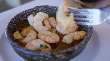 Akdeniz restoranının kırsal bir kasesinde servis edilen karides tabağında, içeride lezzetli bir deniz mahsulü yemeği, sarımsaklı bir masada ve akşam yemeği için bir çatalla servis ediliyor..