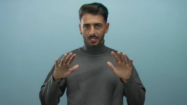 Genç İspanyol adam avuçlarını mavi stüdyoda tutuyor. Odaklanmış bakışlarla nazik bir duruş hareketi yapıyor. Huzur..