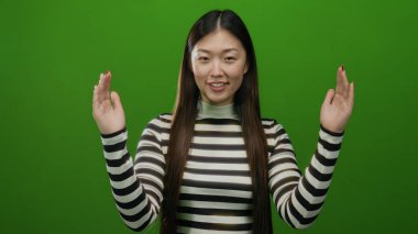 İzole edilmiş yeşil arka planda, çizgili gömlekli, neşeli bir ifade sergileyen, Asyalı özelliklerini ve modern moda anlayışını vurgulayan bir kadın..