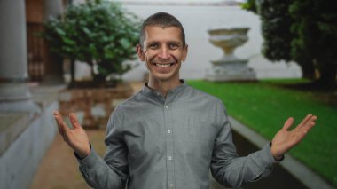 Dışarıda göğsü açık bir şekilde gülümseyen bir adam huzurlu yeşil bir park ortamında gün boyunca mutluluk ve memnuniyet göstermektedir..